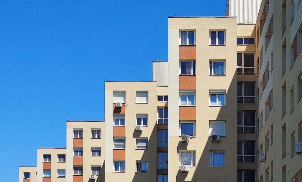 Panelház homlokzata kék ég alatt, több emeletes lakóépület ablakokkal és klímaberendezésekkel. A panellakások iránti kereslet kilőtt az Otthon Start program bejelentése óta.