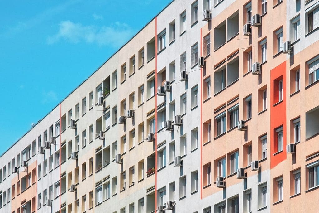 Panelház színes, felújított homlokzattal, számos ablakban és erkélyen klímaberendezésekkel, kék égbolt alatt. Hatalmas a kereslet a panellakásokra az Otthon Start miatt.
