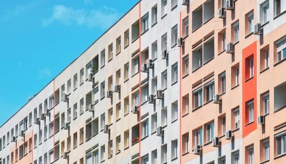 Panelház színes, felújított homlokzattal, számos ablakban és erkélyen klímaberendezésekkel, kék égbolt alatt.