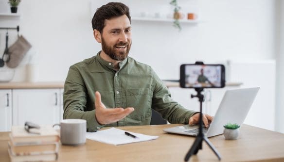 Egy ingatlanközvetítő influenszer videót készít magáról laptop és okostelefon segítségével otthoni környezetben, a személyes márkaépítés és online jelenlét erősítésének céljából.