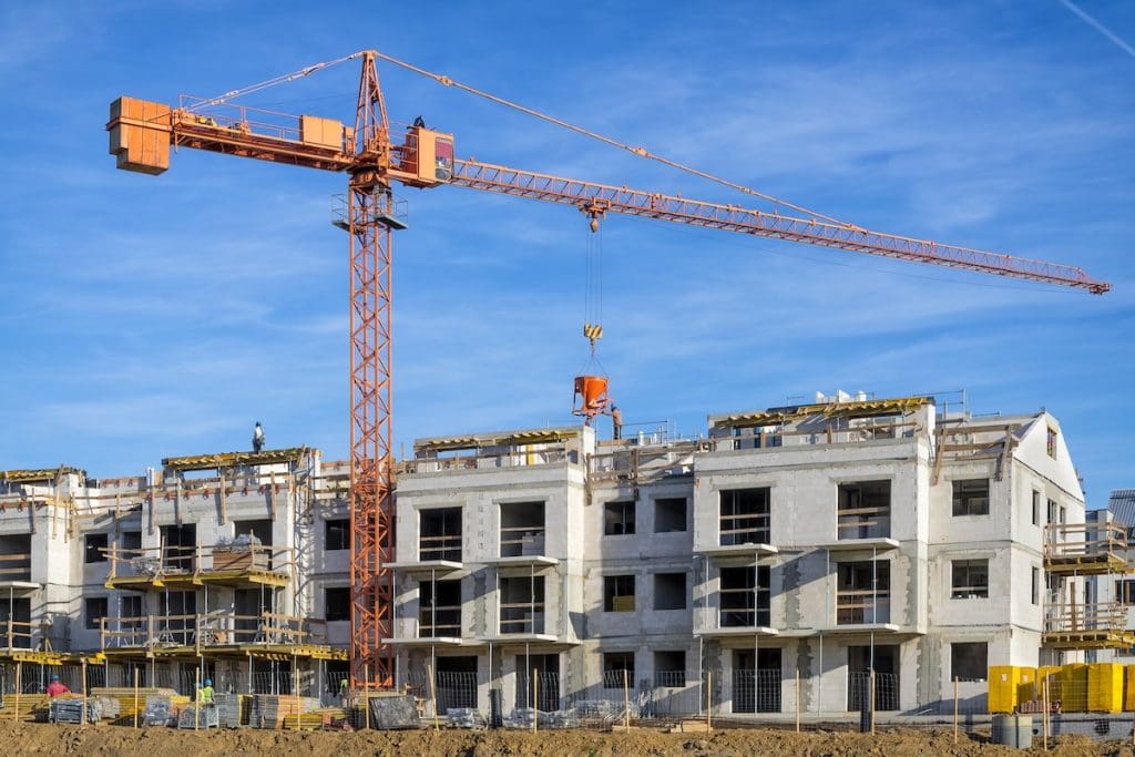 Építés alatt álló új lakópark, mellette daru, a háttérben kék ég. Az épülő lakóparkokra vonatkozik a társasházi építményi jog.