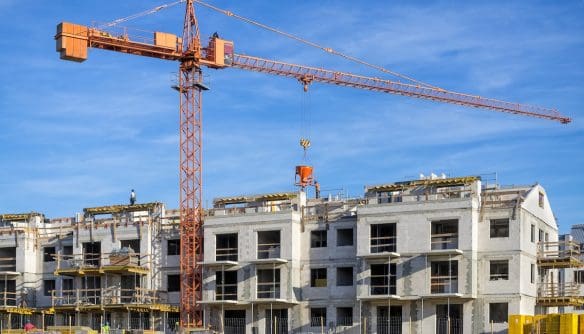 Építés alatt álló új lakópark, mellette daru, a háttérben kék ég. Az épülő lakóparkokra vonatkozik a társasházi építményi jog.