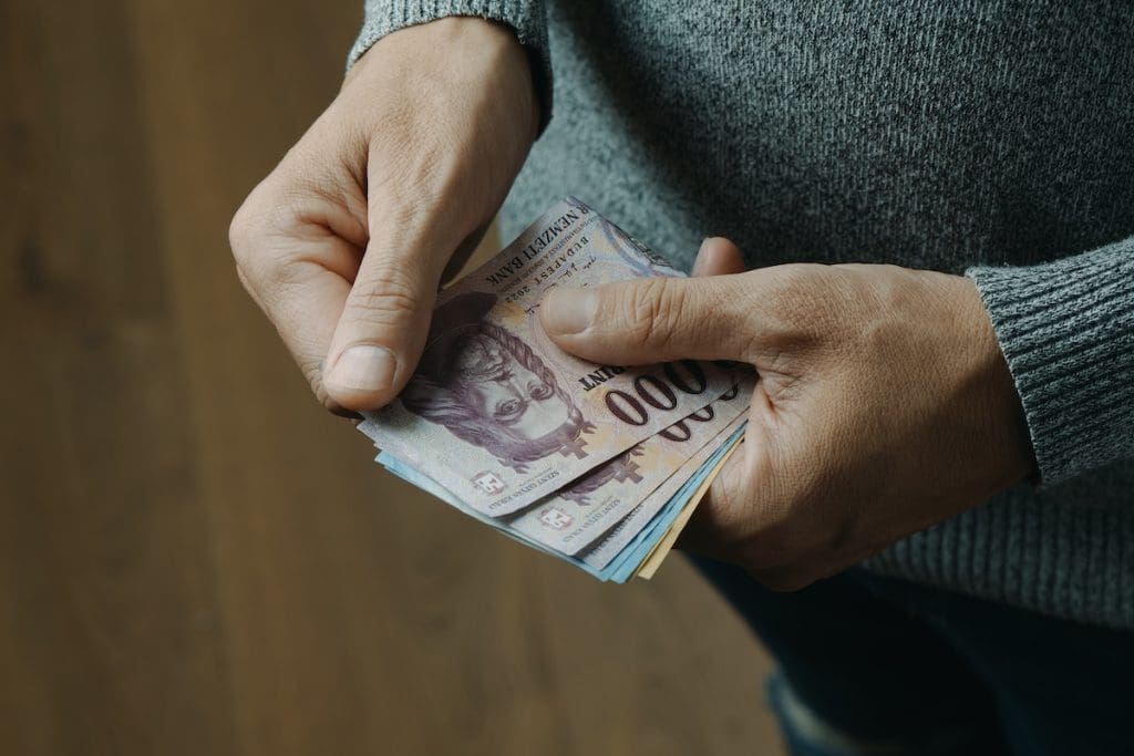 Egy szürke pulóvert viselő férfi a kezében papírpénzt számol, mielőtt átadja a foglaló összegét.