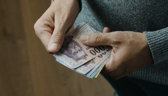 Egy szürke pulóvert viselő férfi a kezében papírpénzt számol, mielőtt átadja a foglaló összegét.