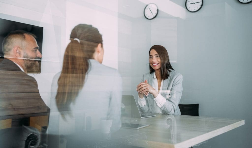 Közjegyző egyeztet a lakásvásárló párral az irodájában. A kép az iroda üvegfalán keresztül készült.