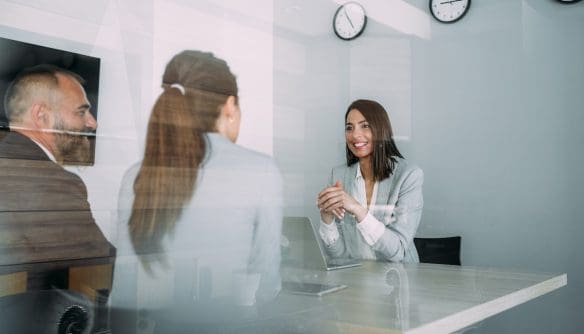 Közjegyző egyeztet a lakásvásárló párral az irodájában. A kép az iroda üvegfalán keresztül készült.