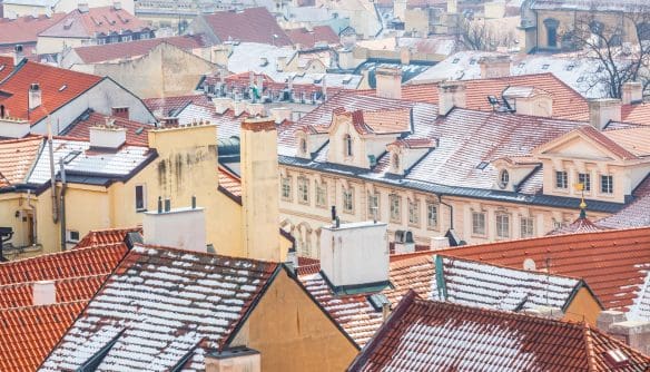 Madártávlati nézet egy sűrűn beépített, történelmi városrészről téli időszakban. A képen egymáshoz szorosan álló, többemeletes lakóépületek láthatók, jellegzetes vörös és barna cseréptetőkkel. A tetőkön vékony hóréteg és havas csíkok fedik a cserepeket, ami enyhe téli hangulatot sugall. Az épületek különböző magasságúak és formájúak, sok kéménnyel, tetőablakkal és díszes tetőfelépítménnyel. A homlokzatok világos színűek – bézs, sárgás és pasztell árnyalatok –, klasszikus, historizáló stílusjegyekkel. A háttérben további tetősorok és épületek halványan elmosódva folytatják a városi látképet. Az összkép egy régi európai nagyváros belső, sűrűn lakott lakónegyedét ábrázolja, nyugodt, hideg téli atmoszférával, emberalakok nélkül.