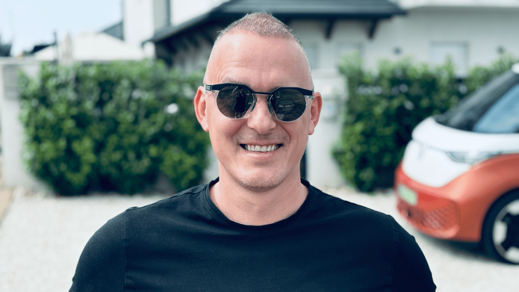 Barna József ingatlanközvetítő portréja. József fekete napszemüvegben és pólóban áll, mögötte elhomályosított utcakép.