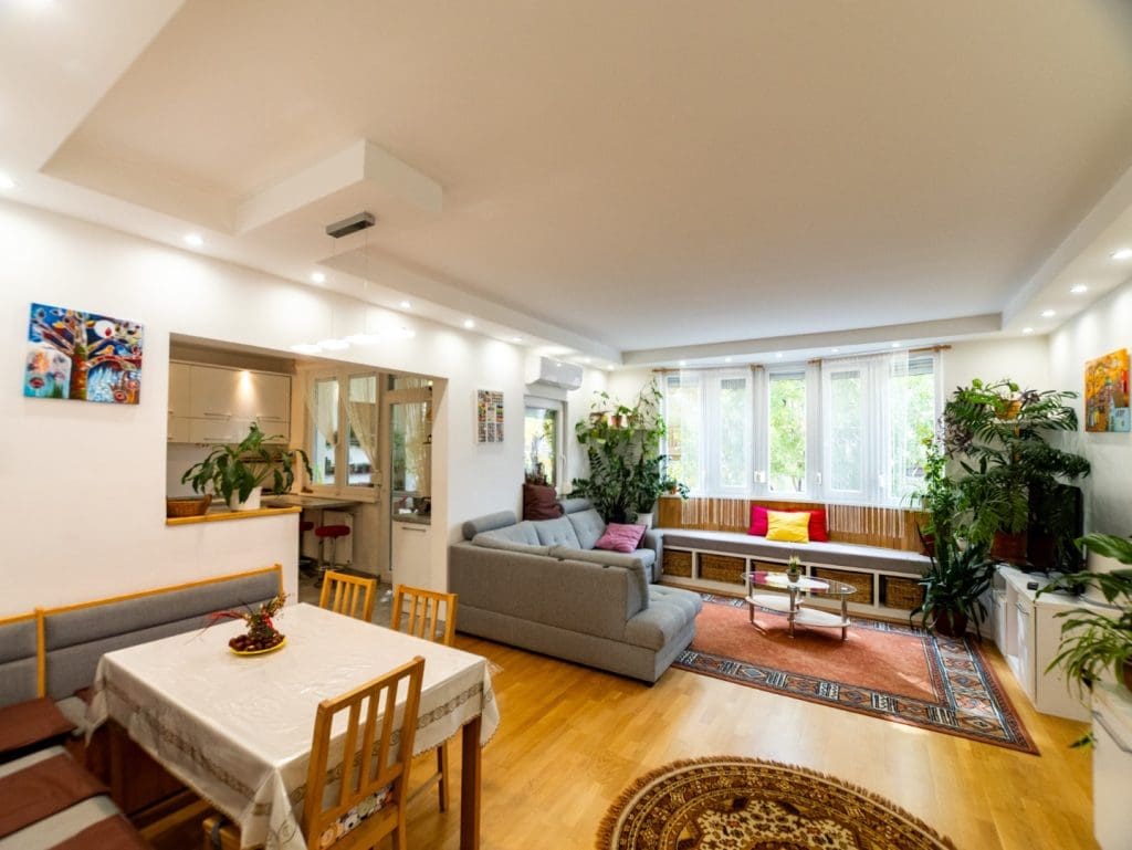 Világos, tágas nappali-étkező amerikai konyhával, nagy ablakfelületekkel, növényekkel és modern berendezéssel.