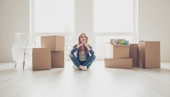 Egy fiatal nő ül törökülésben egy világos, üres lakás világos fa padlóján. Körülötte több kartondoboz látható, némelyik lezárva, mások nyitva, bennük különféle háztartási tárgyakkal. Bal oldalon egy letakart szék utal arra, hogy költözés vagy pakolás zajlik. A háttérben nagy, padlótól mennyezetig érő ablakok engedik be a természetes fényt. A nő az állát a kezére támasztva, kissé felfelé néz, arckifejezése elgondolkodó és bizakodó, mintha az új otthonában tervezgetné a jövőt.