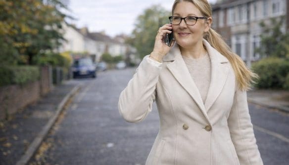 Néber Judit ingatlanközvetítő portréja. Judit egy utcán áll, bézs kötött pulóverben és szövetkabátban, és telefonon beszél.