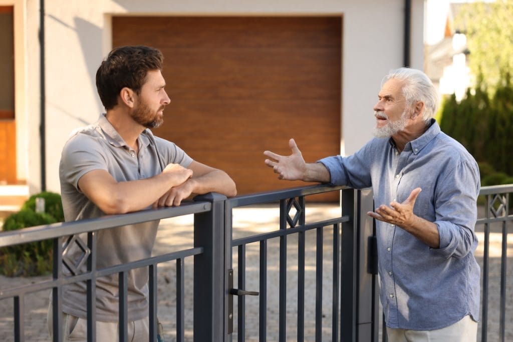 Tulajdonostársak szóváltása egy fém kerítésen keresztül. A közös tulajdonból fakadó vitákat előzi meg az ingatlan használati megállapodás.