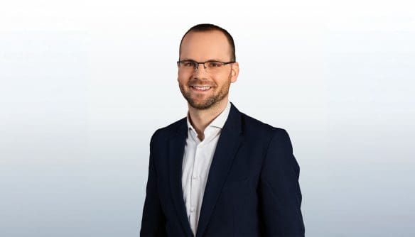 Portré Balogh Alex ingatlanközvetítő szakemberről, szürke színátmenetes háttér előtt.
