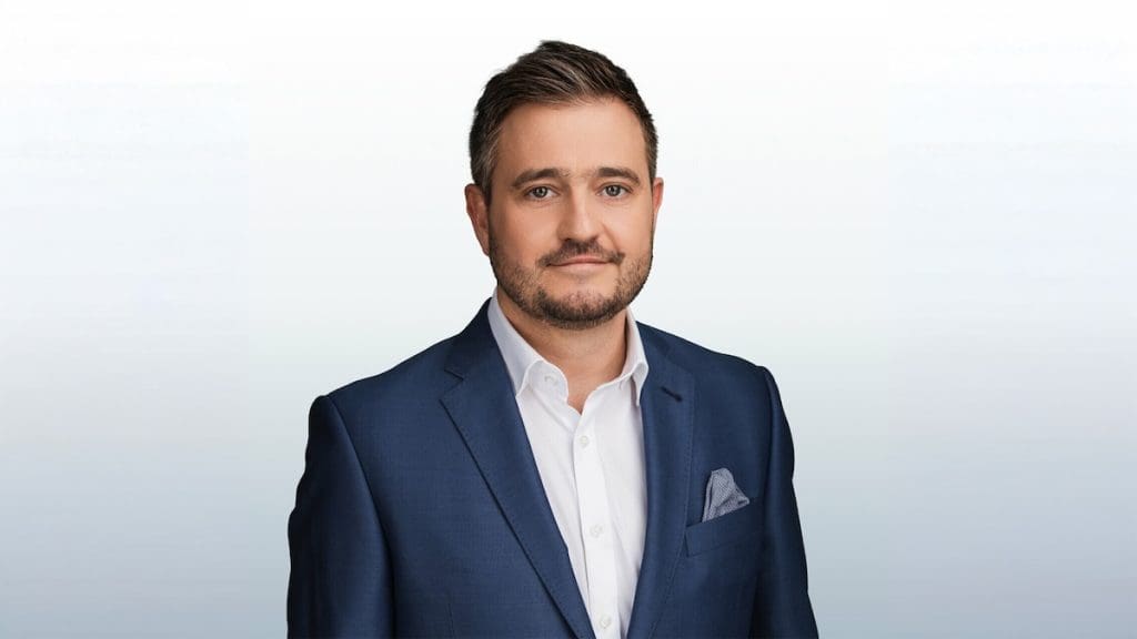 Honos Balázs ingatlanszakértő portréja, szürke színátmenetes háttér előtt.