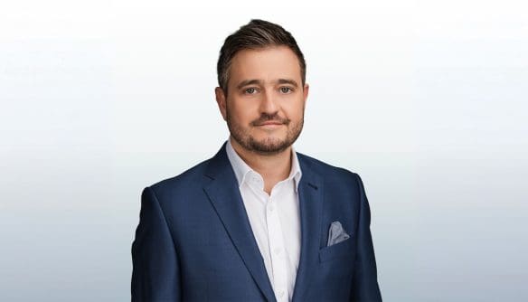 Honos Balázs ingatlanszakértő portréja, szürke színátmenetes háttér előtt.