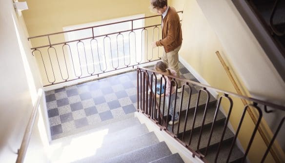 Lakóépület lépcsőháza. Egy apuka és kislánya felülről láthatóak, ahogy sétálnak fel a lépcsőn.